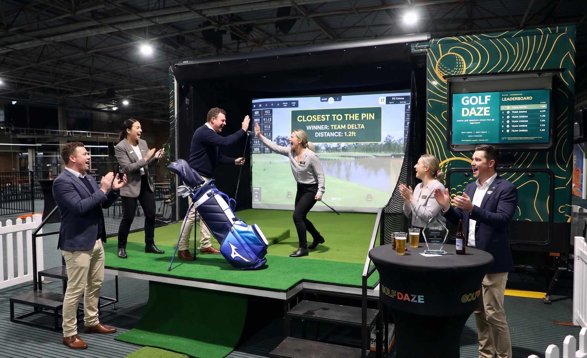 Guests celebrating a closest-to-the-pin win on the Golf Daze leaderboard at a client day, trophy and drinks on the table